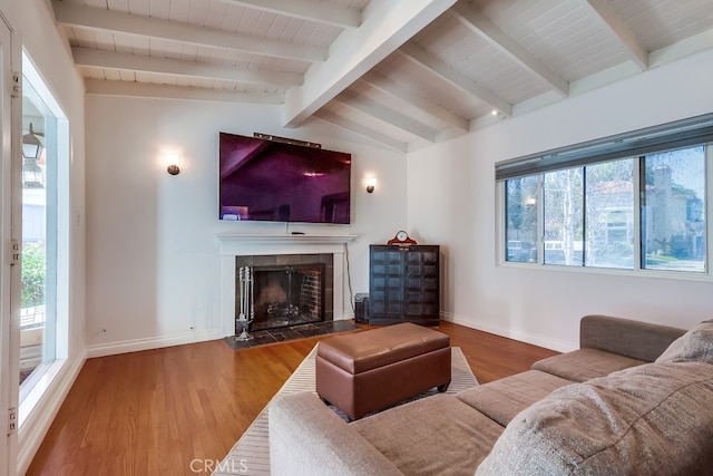 living area featuring a healthy amount of sunlight, lofted ceiling with beams, a tiled fireplace, and wood finished floors