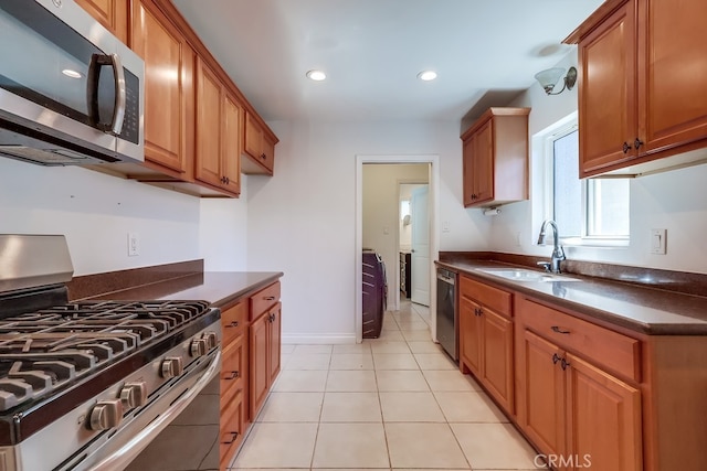 kitchen with appliances with stainless steel finishes, dark countertops, brown cabinetry, and a sink