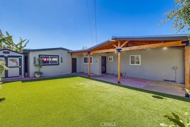 back of property featuring a storage shed, a lawn, a patio, an outdoor structure, and stucco siding