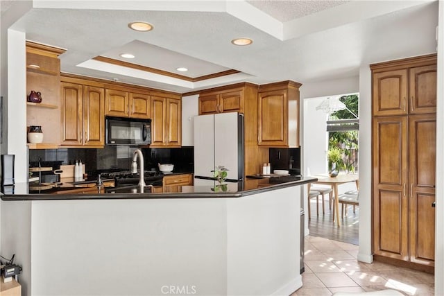 kitchen featuring a tray ceiling, dark countertops, freestanding refrigerator, black microwave, and a peninsula