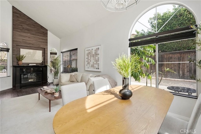 dining space with high vaulted ceiling, a notable chandelier, a fireplace, and wood finished floors