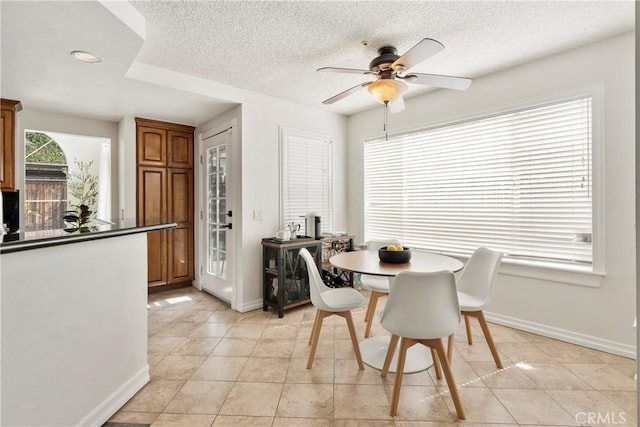 dining room with ceiling fan, a textured ceiling, baseboards, and light tile patterned floors