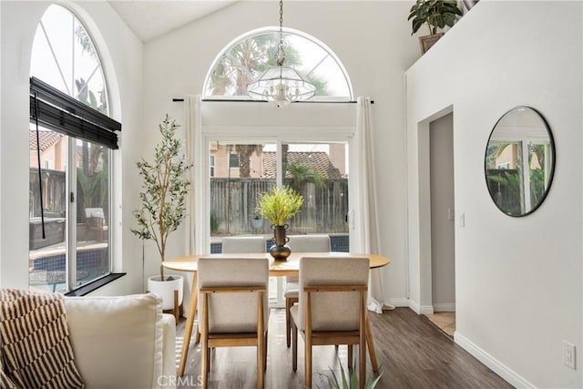 dining space with an inviting chandelier, baseboards, high vaulted ceiling, and wood finished floors