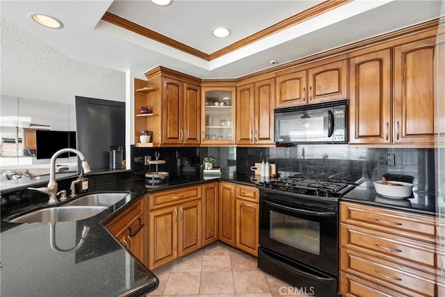 kitchen with brown cabinetry, dark stone countertops, a tray ceiling, black appliances, and a sink