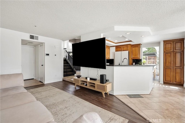 living area with light wood finished floors, visible vents, a raised ceiling, stairway, and recessed lighting