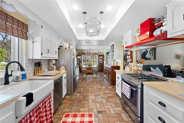 kitchen featuring a tray ceiling, stainless steel appliances, light countertops, backsplash, and a sink