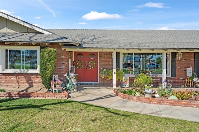 doorway to property with brick siding, a yard, and roof with shingles