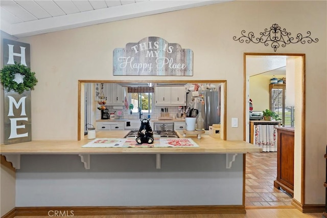 kitchen with a peninsula, a breakfast bar, appliances with stainless steel finishes, beam ceiling, and decorative backsplash