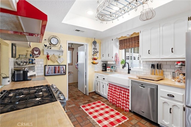 kitchen with stainless steel appliances, tasteful backsplash, a tray ceiling, and white cabinets