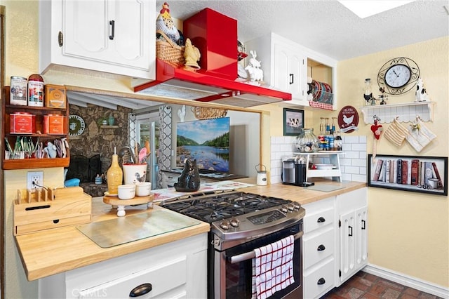 kitchen featuring brick floor, white cabinets, stainless steel gas stove, and backsplash