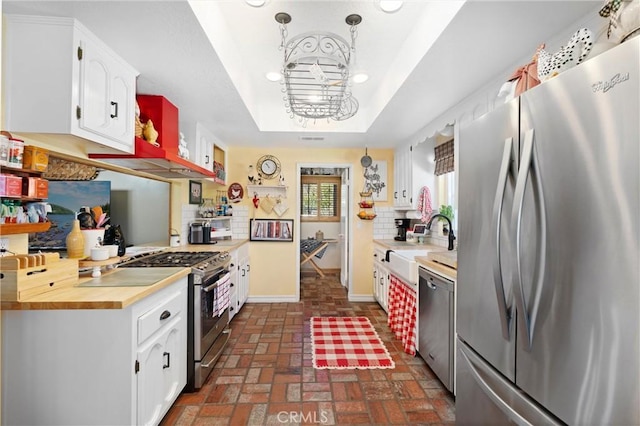 kitchen featuring a raised ceiling, light countertops, decorative backsplash, appliances with stainless steel finishes, and a sink