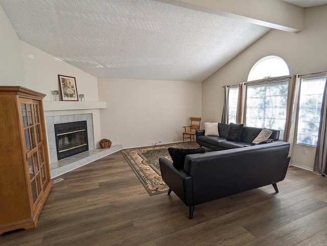 living room with vaulted ceiling with beams, a tiled fireplace, and wood finished floors