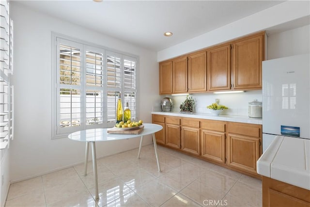 kitchen with tile countertops, light tile patterned floors, recessed lighting, brown cabinetry, and freestanding refrigerator