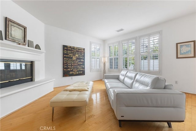 living room featuring light wood-type flooring, a glass covered fireplace, and visible vents