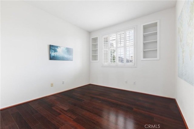 spare room featuring built in shelves, baseboards, and dark wood-type flooring