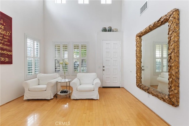 living area featuring hardwood / wood-style floors, a towering ceiling, and visible vents