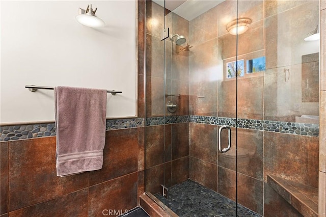 full bath with a stall shower, wainscoting, and tile walls