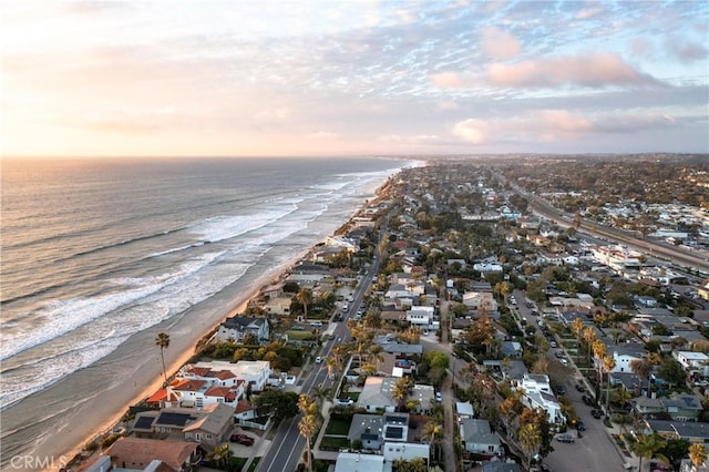 aerial view at dusk featuring a water view and a beach view