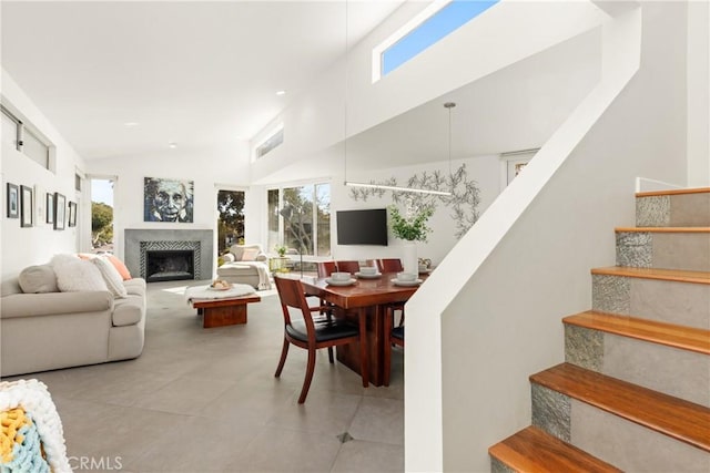 living room featuring a fireplace with raised hearth, high vaulted ceiling, light tile patterned floors, and stairway