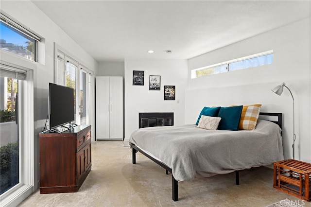 bedroom with multiple windows, concrete floors, a glass covered fireplace, and recessed lighting