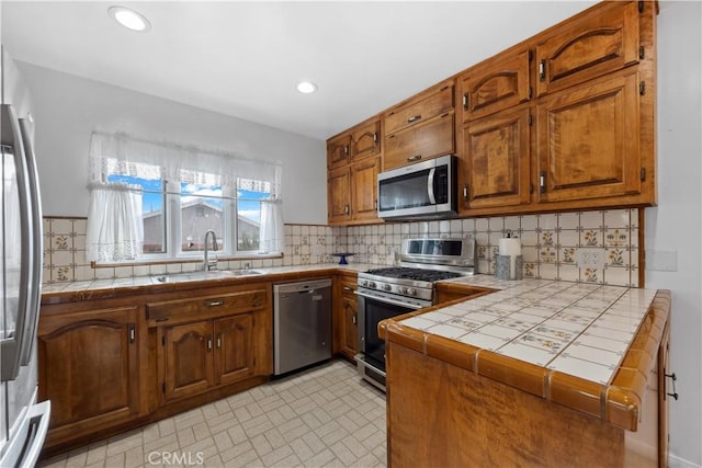 kitchen featuring appliances with stainless steel finishes, tile counters, brown cabinetry, and a sink