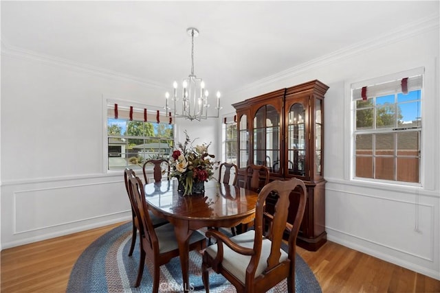 dining area with a wainscoted wall, a notable chandelier, a decorative wall, ornamental molding, and light wood-type flooring