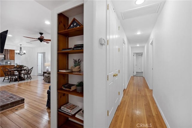 hallway featuring light wood-style floors, built in shelves, and an inviting chandelier