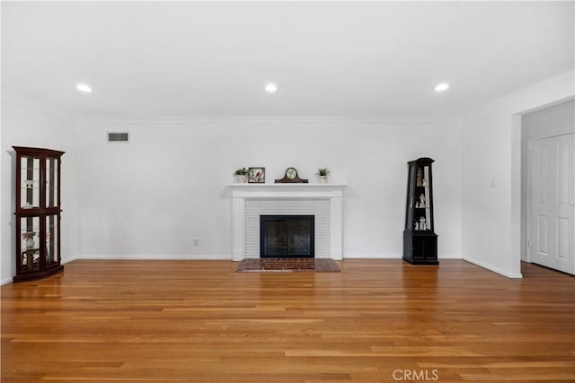 unfurnished living room with crown molding, visible vents, a fireplace, and light wood finished floors