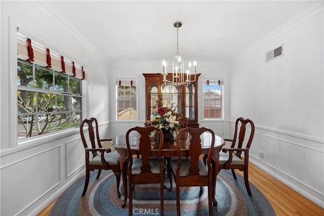 dining area featuring a wainscoted wall, visible vents, a notable chandelier, and wood finished floors