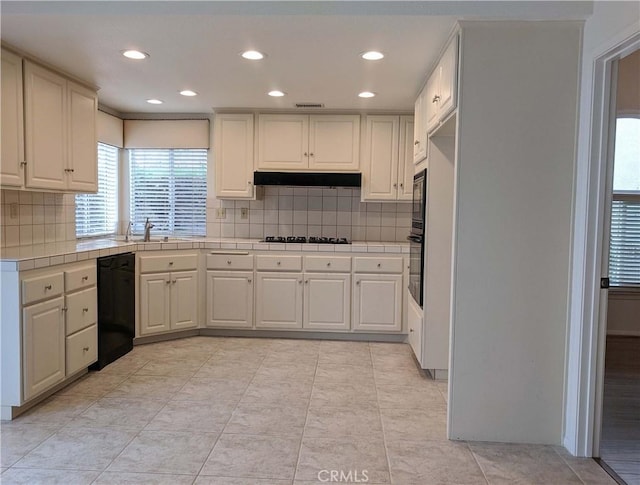 kitchen featuring tile countertops, under cabinet range hood, visible vents, decorative backsplash, and black appliances