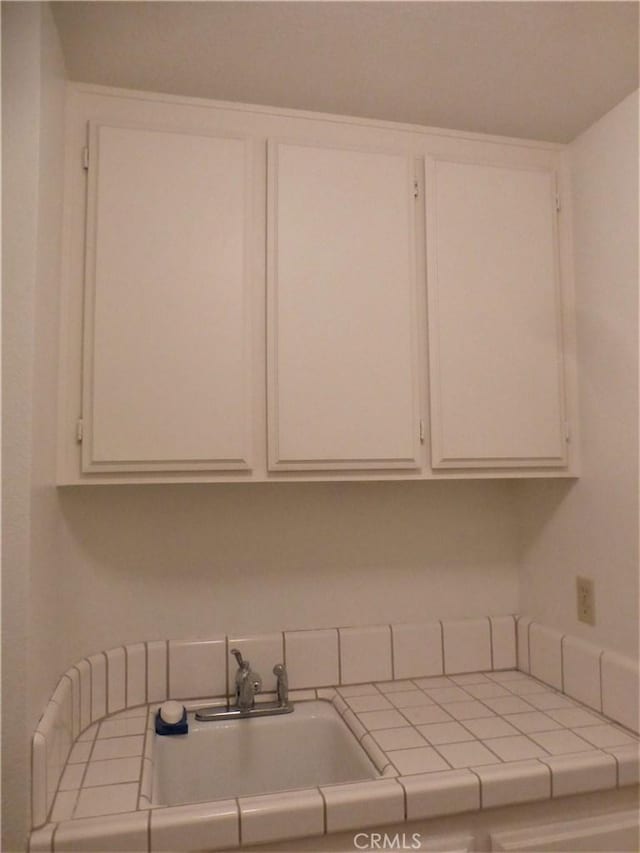 kitchen featuring white cabinetry, a sink, and tile countertops