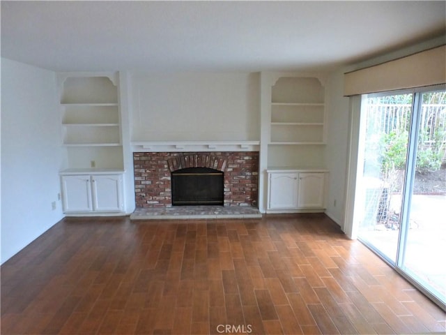 unfurnished living room featuring built in shelves, a brick fireplace, and wood finished floors