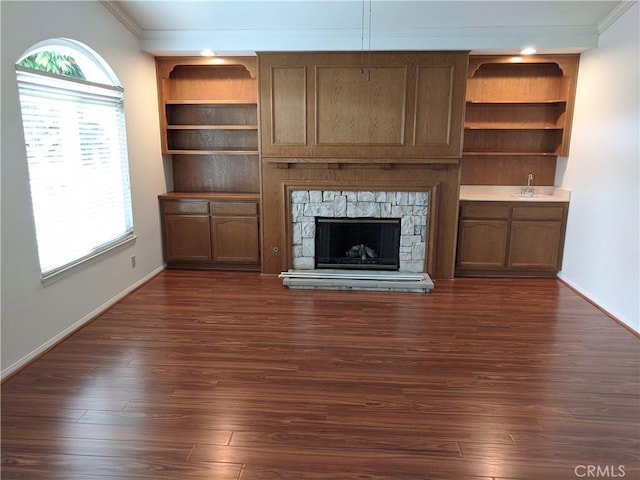 unfurnished living room with dark wood-style floors, baseboards, ornamental molding, and a stone fireplace