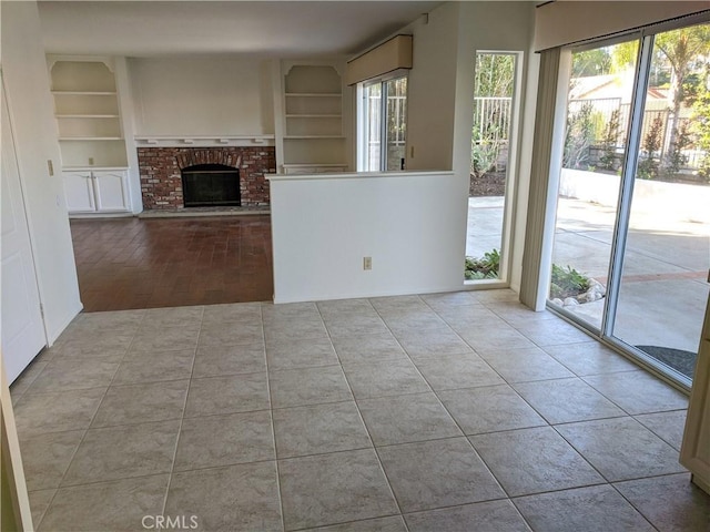 unfurnished living room featuring a brick fireplace, tile patterned floors, and built in features