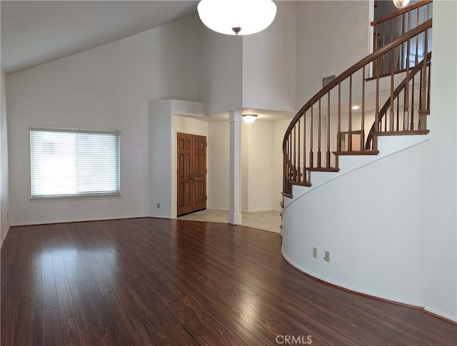 unfurnished living room with stairway, decorative columns, high vaulted ceiling, and wood finished floors