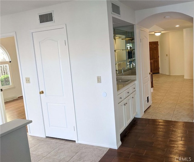 corridor with arched walkways, visible vents, a sink, and light wood finished floors