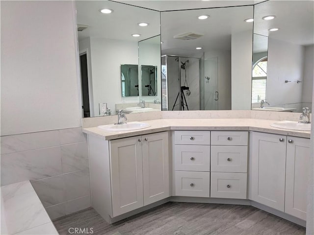 bathroom featuring visible vents, a sink, a shower stall, and double vanity