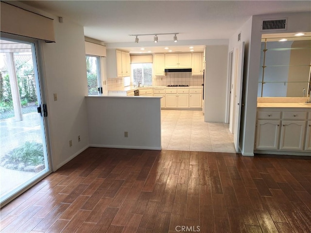 kitchen featuring cooktop, visible vents, decorative backsplash, wood finished floors, and under cabinet range hood