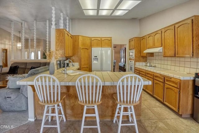 kitchen featuring tile counters, white appliances, a sink, and under cabinet range hood