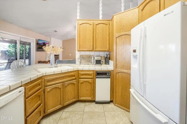 kitchen with white appliances, tasteful backsplash, light tile patterned floors, a peninsula, and a sink