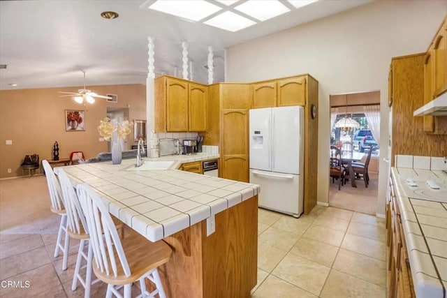 kitchen featuring tile counters, lofted ceiling with skylight, freestanding refrigerator, a peninsula, and a sink