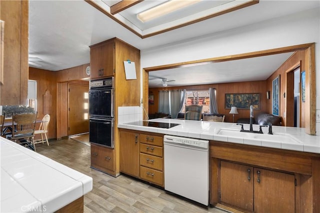 kitchen with white dishwasher, a sink, tile counters, and brown cabinets