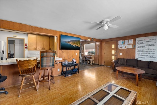 living room featuring a ceiling fan, wood walls, and light wood finished floors