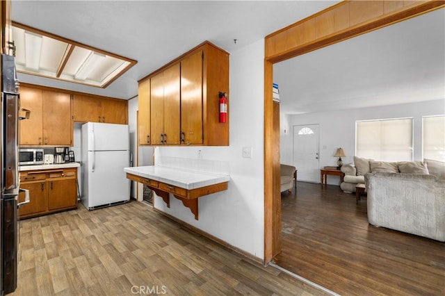 kitchen featuring brown cabinetry, tile countertops, stainless steel microwave, wood finished floors, and freestanding refrigerator