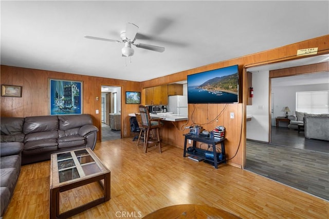 living area featuring a ceiling fan, wooden walls, and wood finished floors