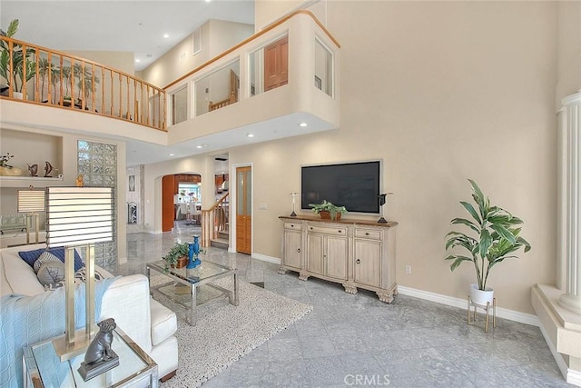 living area featuring arched walkways, granite finish floor, a high ceiling, baseboards, and stairs