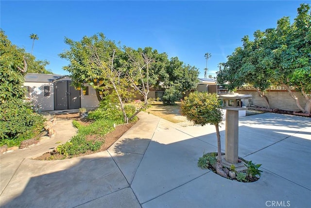 view of property hidden behind natural elements featuring an outbuilding, a storage unit, a patio area, and fence