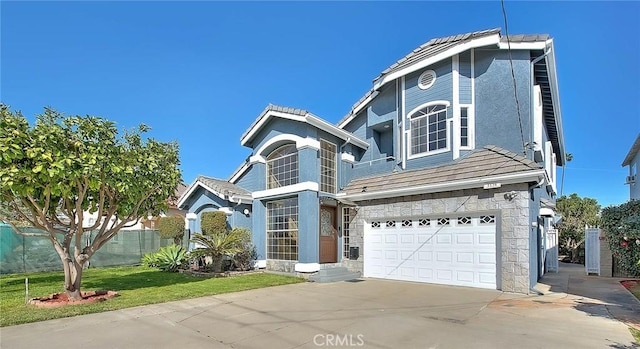 traditional home featuring driveway, a garage, stone siding, fence, and a front yard