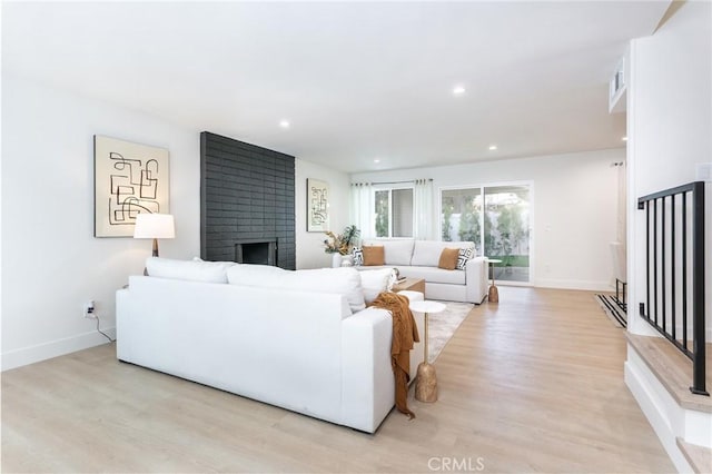 living room featuring light wood finished floors, a fireplace, baseboards, and recessed lighting