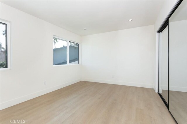 unfurnished bedroom with light wood finished floors, baseboards, a closet, and recessed lighting